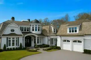 Front view of a Shingle Style Coastal home featuring classic shingle siding, natural wood roofing, arched dormers, white trim, and symmetrical architecture